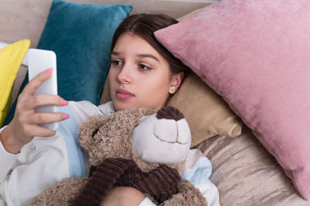 sad teenage girl using smartphone and holding teddy bearの写真素材