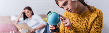 sad teenage girl looking at globe with blurred mother on background, banner