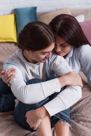 caring mother embracing smiling teenage daughter in bedroomの写真素材
