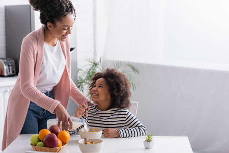 joyful african american kid holding spoon while looking at smiling mother in kitchenの写真素材