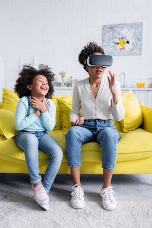 excited african american kid laughing near mother gesturing in vr headsetの写真素材