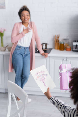 african american child holding happy mothers day card near mom holding hand on chest on blurred...