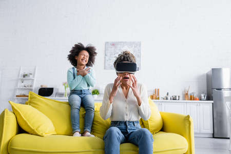 scared african american woman in v headset gesturing near laughing daughterの写真素材