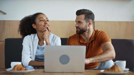 cheerful interracial freelancers near laptop and breakfast in cafe