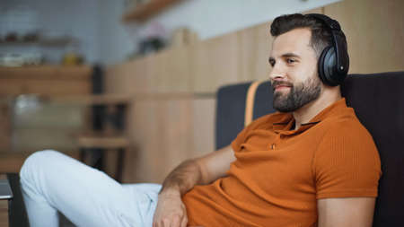 pleased man in wireless headphones listening music and chilling in cafe
