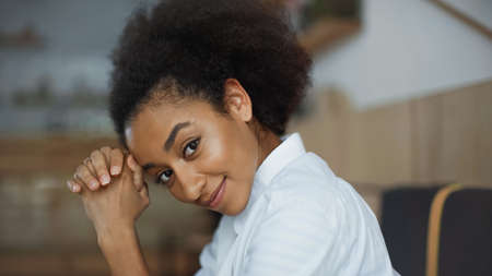 cheerful african american woman with clenched hands smiling and looking at camera in cafeの写真素材
