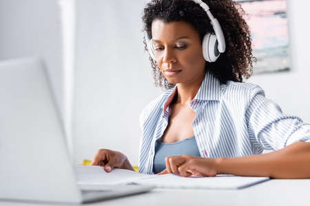African american freelancer in headphones working near laptop on blurred foreground