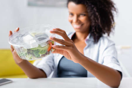 Takeaway salad in hands of african american woman on blurred background