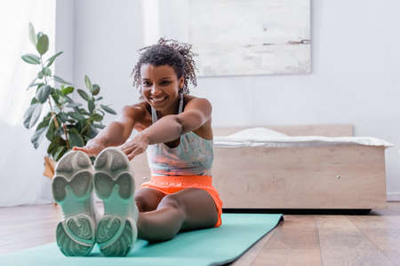 Cheerful african american woman stretching on floor in bedroom