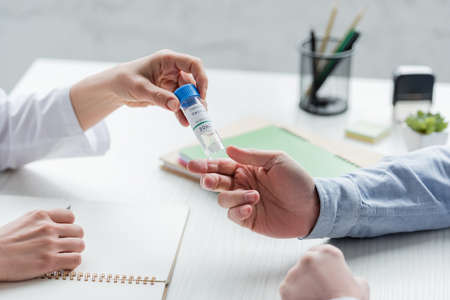 Cropped view of doctor holding coronavirus vaccine near patient and notebookの写真素材