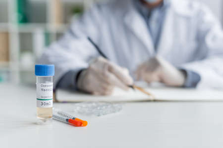 Cropped view of coronavirus vaccine and syringes near doctor on blurred background in hospital