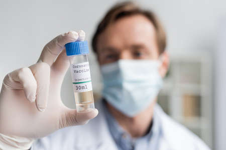 Jar with vaccine in hand of doctor in latex glove on blurred backgroundの写真素材