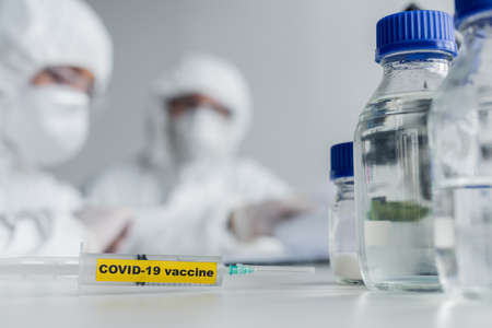 Syringe with covid-19 vaccine lettering near scientists in laboratoryの写真素材