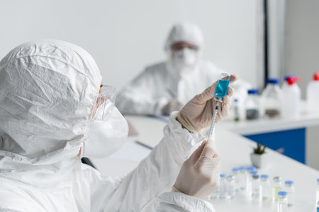 Scientist picking up vaccine in syringe near colleague on blurred background