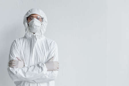 Scientist in hazmat suit and protective goggles looking at camera with crossed arms