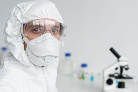 Scientist in goggles and hazmat suit looking at camera in laboratory
