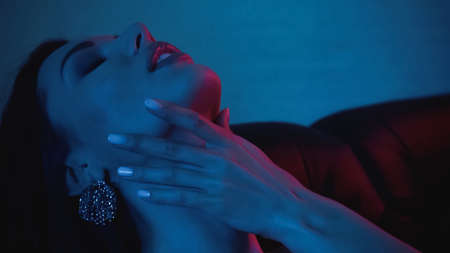 red lighting on seductive woman touching neck on blue