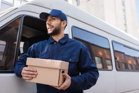 happy arabian postman looking away while standing with parcel near carの写真素材