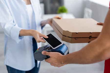 cropped view of delivery man holding payment terminal and pizza boxes near woman with mobile phone