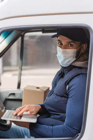 muslim delivery man in medical mask typing on laptop in carの写真素材