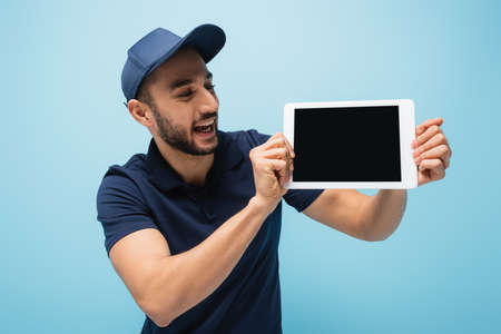 excited arabian courier showing digital tablet with blank screen isolated on blueの写真素材