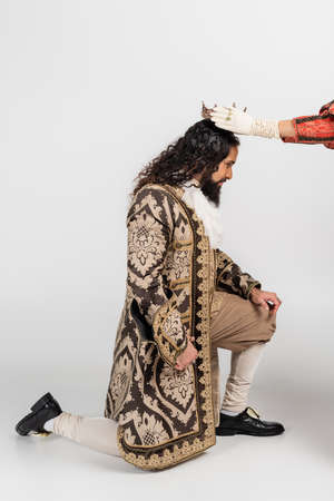queen wearing crown on hispanic king in medieval clothing standing on knee on white