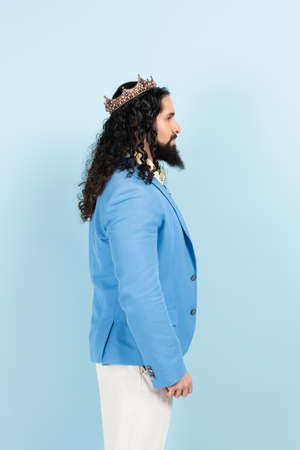 side view of bearded hispanic man in jacket and crown isolated on blueの写真素材