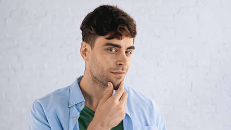pensive man touching chin while looking at camera