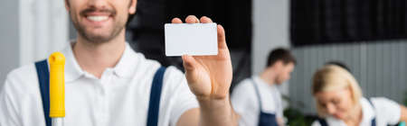 Empty card in hand of smiling cleaner on blurred background in office, banner
