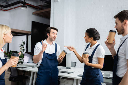 African american cleaner with coffee to go pointing at colleague in office