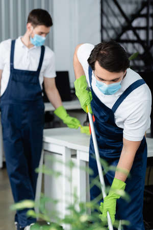 Cleaner in protective mask holding mop in office
