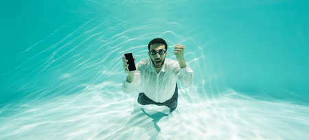 Excited muslim businessman in goggles showing yes gesture and smartphone in swimming pool, bannerの写真素材