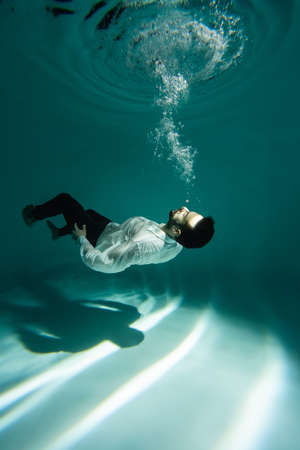 Arabian man in formal wear swimming near bubbles of air underwaterの写真素材