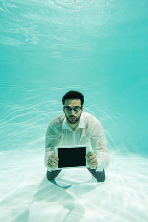 Arabian manager in goggles holding digital tablet underwater
