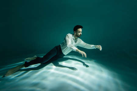 Bearded arabian man swimming underwater in pool with lightの写真素材