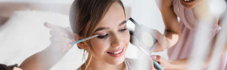 bridesmaids applying makeup on pretty bride, blurred foreground, bannerの写真素材