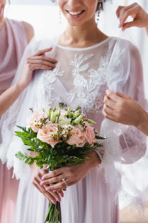 cropped view of african american bride with wedding bouquet near bridesmaids adjusting her veil