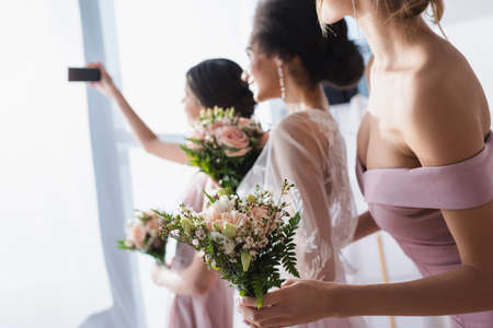 bride taking selfie with interracial bridesmaids holding wedding bouquets, blurred backgroundの写真素材