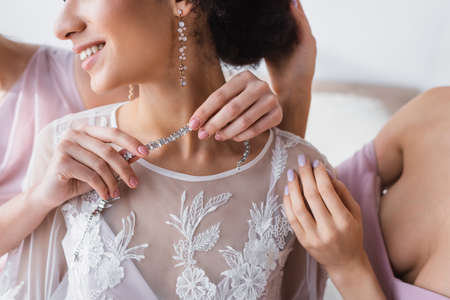 cropped view of bridesmaid holding necklace near smiling african american brideの写真素材