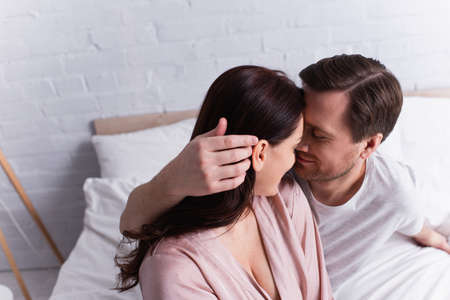 Adult man touching hair of brunette wife in pajama on bed