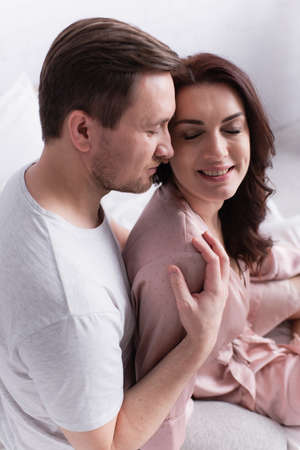 High angle view of man hugging positive wife in pajama on bed