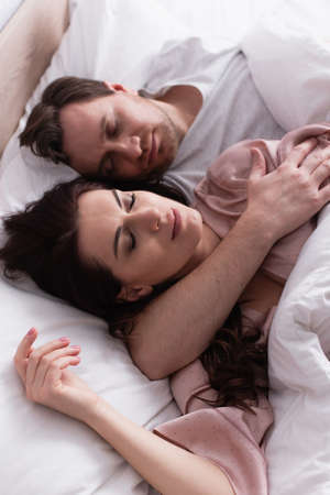 Brunette woman sleeping near husband on blurred background on bedの写真素材