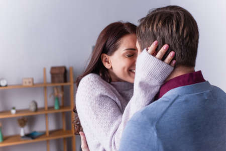 Smiling woman in sweater hugging man at home
