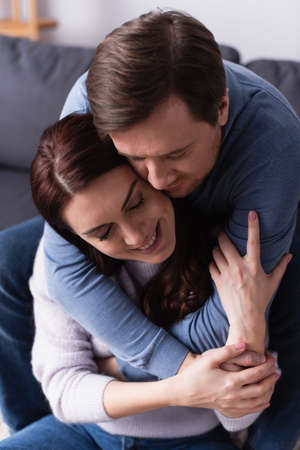 Man hugging happy brunette wife at home