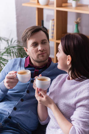 Man with cup of coffee looking at wife on blurred foregroundの写真素材