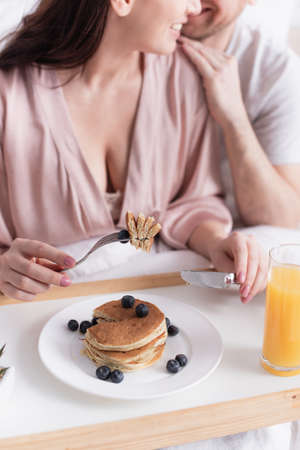 Cropped view of woman holding cutlery near pancakes with berries, orange juice and husband on...