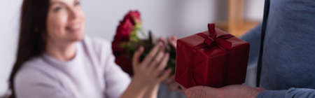 Man holding present and giving flowers to wife on blurred background, bannerの写真素材