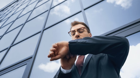 low angle view of businessman in glasses looking at wristwatch outsideの写真素材