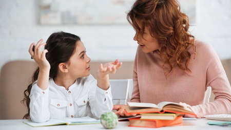 Girl with pen talking to mother while doing homework