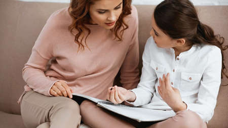 Woman helping daughter with pen and notebook during home educationの写真素材
